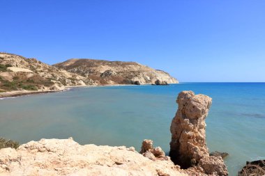 Akdeniz suyunun Afrodit Körfezi 'nde taş kayalıklı Afrodit Sahili güneşli bir arka planda mavi gökyüzü Kıbrıs' ta Petra tu Romiou