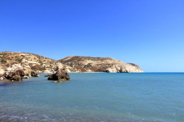 Akdeniz suyunun Afrodit Körfezi 'nde taş kayalıklı Afrodit Sahili güneşli bir arka planda mavi gökyüzü Kıbrıs' ta Petra tu Romiou