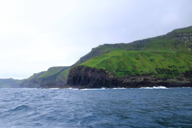 a view to Mykines Island showcasing towering cliffs surrounded by the expansive North Atlantic Ocean, Faroe Islands, Denmark