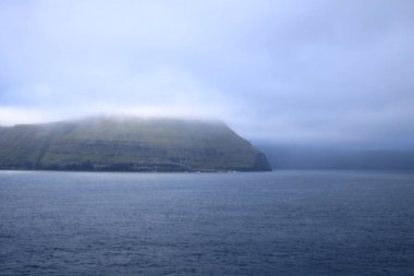 dramatic island emerges from the tranquil waters of the Faroe Islands, shrouded in a thick layer of fog