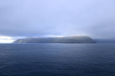 dramatic island emerges from the tranquil waters of the Faroe Islands, shrouded in a thick layer of fog