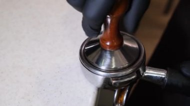 Kahveleri tazeleyen bir baristanın üzerini kapatın. Profesyonel barista çalışanı kahve çekirdeklerini öğütmek için öğütücü makine kullanıyor ve kahve dükkanında sıcak içecek yapmak için portafilter içine bastırıyor.