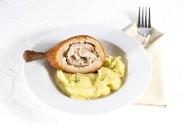 Tereyağı ve otla doldurulmuş ekmek kırıntılarına kesilmiş tavuk pirzolası. Beyaz arka planda, yatay olarak patates püresiyle servis edilmiş.