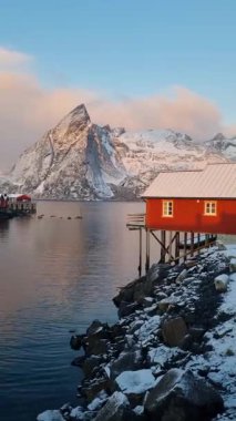 Kışın Lofoten adalarında geleneksel rorbu evleri olan Reine köyü. Kuzey Norveç 'teki Reinebringen Dağı ve donmuş deniz suyu üzerinde kırmızı ahşap balıkçı kulübeleriyle İskandinav manzarası.