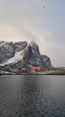 Kış mevsiminde Lofoten adalarındaki muhteşem manzara. Karlı dağları olan etkileyici bir kış manzarası, geleneksel kırmızı balıkçı kulübeleri, rorbu. 