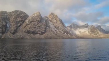 Norveç 'in Lofoten Adaları' ndaki Reine köyünün üzerindeki güzel karlı dağlar, kışın güneş doğarken kısmen donmuş fiyort ve gökkuşağı ile. Şafakta karlı kayalar ve denizin üzerinde dramatik bir gökyüzü