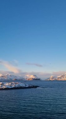Kuzey Norveç 'in Lofoten bölgesinde kısmen donmuş bir göl ve dramatik kış atmosferiyle karla kaplı dağ manzarası