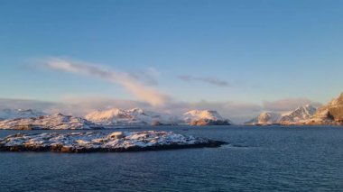 Kuzey Norveç 'in Lofoten bölgesinde kısmen donmuş bir göl ve dramatik kış atmosferiyle karla kaplı dağ manzarası