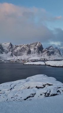 Norveç 'in Lofoten Adaları' ndaki Reine kasabasında kışın karla kaplı dağla kıyı şeridindeki kuzeyli balıkçı köyünün güzel manzarası