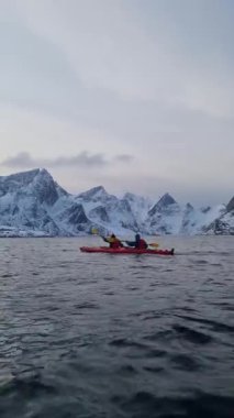 Turistler Norveç Denizi üzerinde kanoyla seyahat ederler. Hamnoy köyü, Lofoten Adaları. Resimli kış manzarası kutup dairesi üzerinde. Seyahat konsepti arka planı.