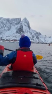 Turistler Norveç Denizi üzerinde kanoyla seyahat ederler. Hamnoy köyü, Lofoten Adaları. Resimli kış manzarası kutup dairesi üzerinde. Seyahat konsepti arka planı.