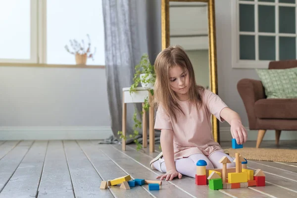 Cute girl plays on the floor with a wooden constructor