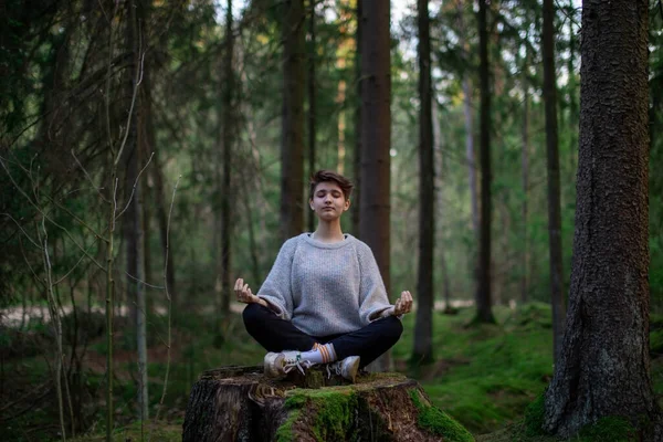 A teenage girl with short hair is doing yoga in a green forest. The concept of a healthy lifestyle and unity with nature — Stock Photo, Image