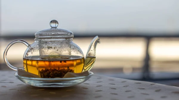 Transparente Teekanne mit heißem grünen Naturtee auf dem Tisch. Großes Fenster. — Stockfoto