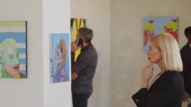 Sanat galerisinde çenesinin altında duran ve duvardaki soyut resmi inceleyen orta yaşlı güzel bir kadının yan görüntüsü.