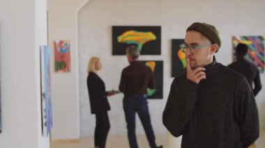 Galeride çağdaş sanat sergisini ziyaret ederken duvardaki tabloyu inceden inceye inceleyen beyaz bir genç.