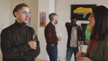 Genç bir adam ve kadının şampanya bardakları tutarken ve sanat galerisindeki açılış partisinde sohbet ederken belini kaldır.