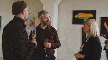 İki neşeli adam ve orta yaşlı kadın galeri müdürünün açılış partisinde içki içip sohbet ederken çekilmiş.