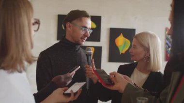 Galeride açılan sanat sergisinde çok ırklı gazetecilere röportaj veren genç erkek sanatçı