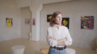 Kolları çapraz duran ve modern sanat galerisinde kameraya poz veren genç bir kadının portre fotoğrafını yakınlaştırın.