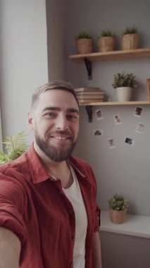 Dikey el kamerasıyla çekilen, sakallı ve elini uzatmış neşeli, beyaz bir adamın kamera karşısında canlı bir şekilde sohbet ederken, el sallayarak selam verirken ve gülümserken.