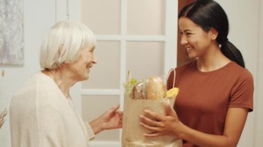 Genç Asyalı kadın bakıcı evdeki emeklilere yiyecek getiriyor. Mutlu son sınıf kadınları ona sarılıp teşekkür ediyor.