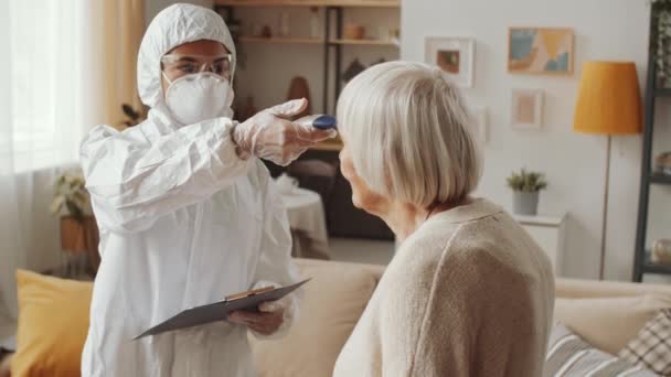 Ärztin Schutzanzug Misst Temperatur Einer Älteren Frau Mit Infrarot Thermometer — Stockvideo