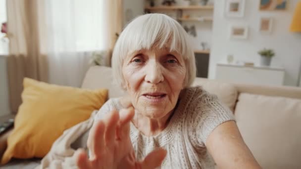 Yaşlı Gri Saçlı Kadın Oturma Odasındaki Kanepede Otururken Kameraya Sallıyor — Stok video