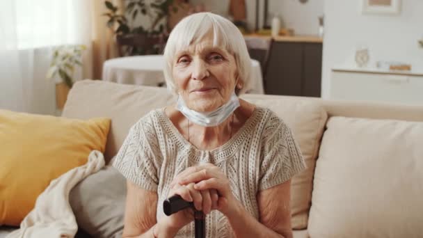 Portret Pozytywnej Starszej Kobiety Masce Ochronnej Pod Podbródkiem Siedzącej Kanapie — Wideo stockowe