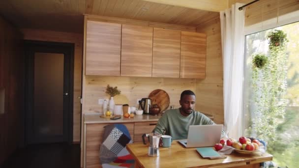 在乡间别墅的厨房桌子上 用笔记本电脑打字和喝咖啡的年轻非洲裔美国人的镜头把镜头放大 — 图库视频影像