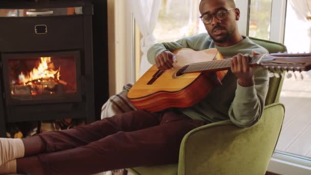 Junger Afroamerikaner Sitzt Kamin Gemütlichem Landhaus Spielt Gitarre Und Singt — Stockvideo