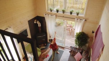 Spor kıyafetli, çıplak ayaklı bir kadının tatil evindeki minderde yoga çalışmasının yüksek açılı görüntüsü.