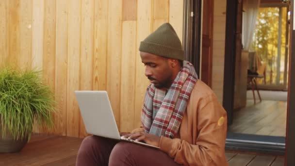 Joven Afroamericano Sentado Aire Libre Porche Casa Madera Escribiendo Portátil — Vídeo de stock