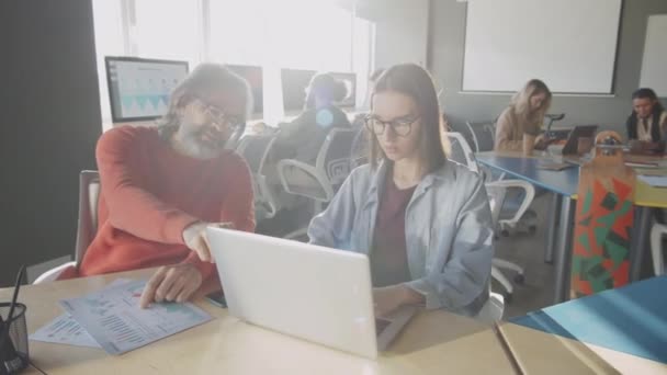 시니어 사업가가 사무실의 책상에 동안젊은 동료와 노트북으로 프로젝트에 이야기하는 — 비디오