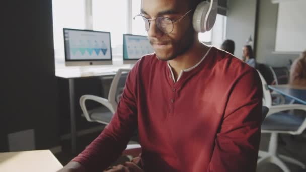 기사보기 헤드폰을 착용하고 사무실에서 일하는 잘생긴 남성의 모습을 가까이서 수있다 — 비디오