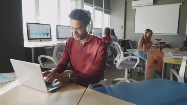 헤드폰을 현대의 사무실의 책상에서 노트북으로 일하는 잘생긴 사업가 — 비디오