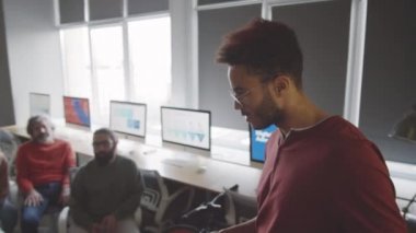 Genç yakışıklı melez adam iş toplantısında sunum yaparken çeşitli meslektaşlarına projeksiyon ekranında bilgi veriyor.