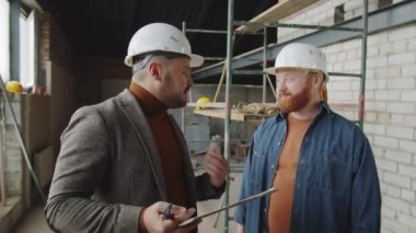 Mimar ve miğferli erkek müşterilerin yeni tamamlanmamış apartman dairesinde dikilip tartıştıkları belden yukarı pozlar.