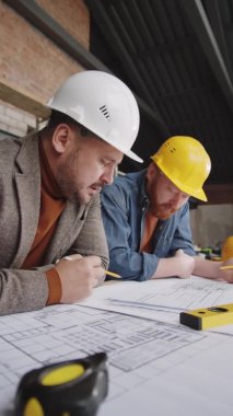 İnşaat alanında çalışırken iki profesyonel mimarın masa planını tartışırken dikey çekimi.