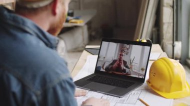 Erkek mimarın, inşaat alanında çalışırken bilgisayardan erkek meslektaşıyla iş görüşmesi yaparken çekilmiş omuz fotoğrafı.