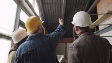 Erkek ve kadın mimarlardan oluşan bir ekibin arka planı yeni tamamlanmamış bir dairede tavan inşaatına işaret ediyor ve iş günü boyunca tartışıyorlar.