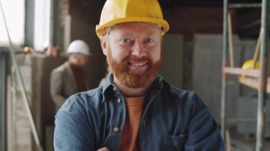İnşaat alanında durup kameraya bakıp gülümseyen kasklı mutlu sakallı erkek mimarın göğüs portresi.