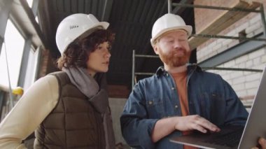 İnşaat alanında yan yana dizilmiş profesyonel erkek ve kadın mimarların dizüstü bilgisayardan bir şey tartışırken belini kaldır.