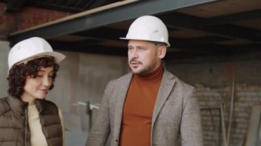 Kadın meslektaşımla inşaat alanında yürüyüp iş hakkında tartışan sert şapkalı profesyonel erkek mühendis.