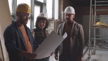 İnşaat alanında birlikte çalışırken iki erkek mimar ve kadın meslektaşlarından oluşan belden yukarı bir çekim.
