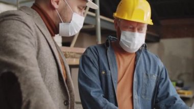 Tek kullanımlık yüz maskeleri takmış iki erkek mimar dizüstü bilgisayardaki projeyi tartışırken aynı inşaat alanında COVid-19 salgını sırasında birlikte çalışıyorlar.