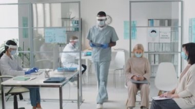 Siyahi doktor asistanı koruyucu yüz maskesi ve ekran karşılama kadın hasta bekleme odasında, tıbbi geçmiş alarak ve covid-19 salgını sırasında onu doktor ofisinde oturma