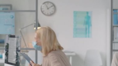 Korunaklı maske takan Afro-Amerikalı doktor, ekran ve eldivenler tıbbi geçmişi okuyor ve Coronavirus pandemisi sırasında klinikteki hastalarla çalışırken kadınlara danışmanlık yapıyor.