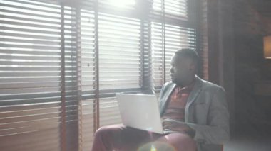 Genç Afro-Amerikalı iş adamının portre fotoğrafını yakınlaştırın. Günlük kıyafetlerini giyip ev bilgisayarında çalışırken özgüvenle kameraya bakın.