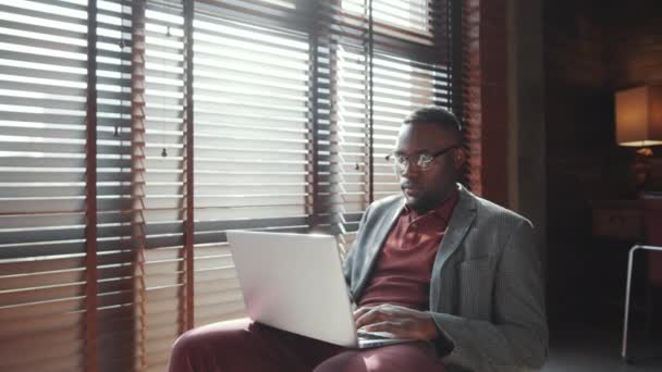 身着时髦休闲装 戴眼镜 头戴百叶窗 在笔记本电脑上打字的年轻非洲裔美国商人在自家办公室工作时 镜头放大 — 图库视频影像